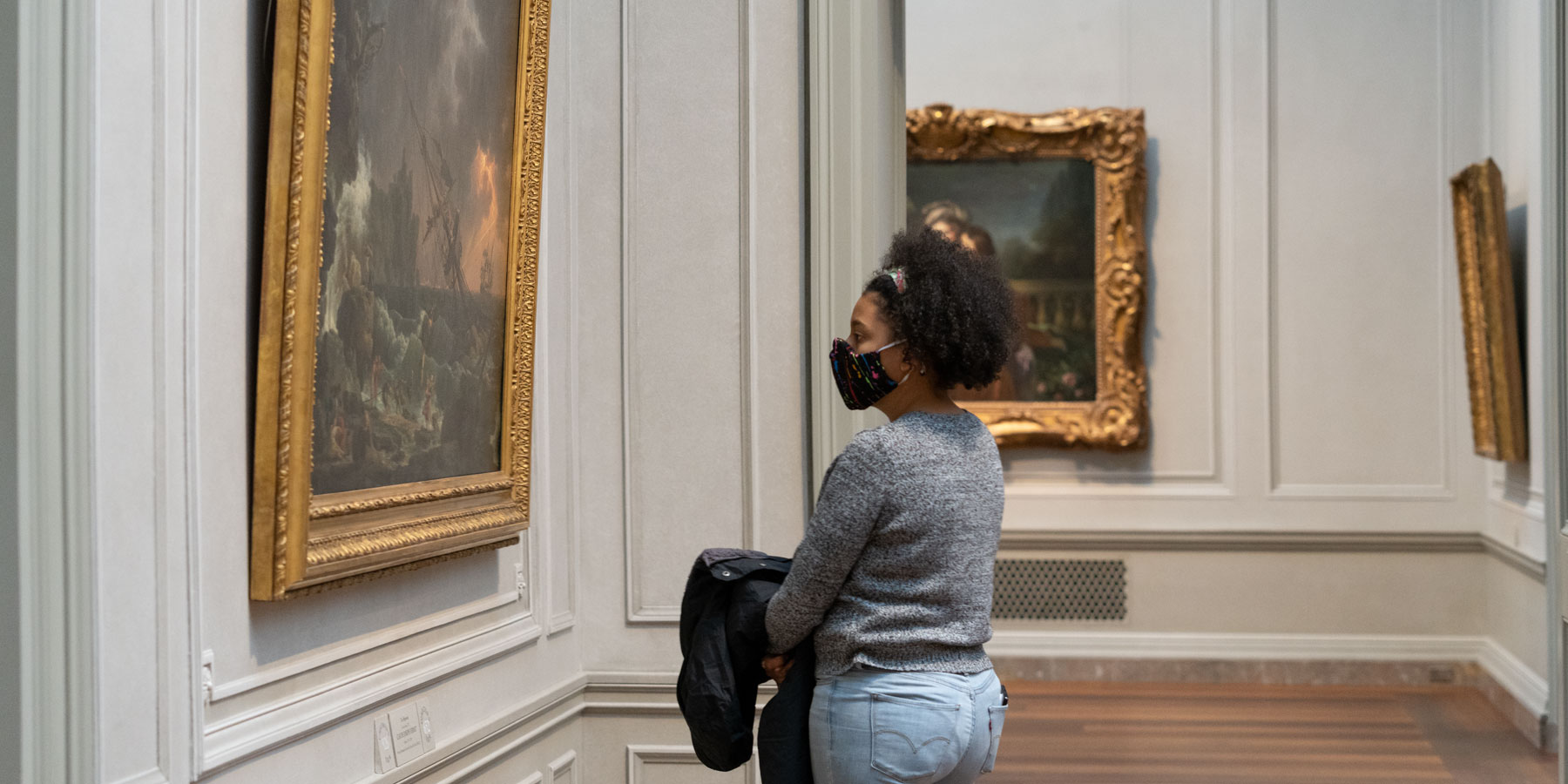 A woman with a facemask on is looking at a painting in the National Gallery.
