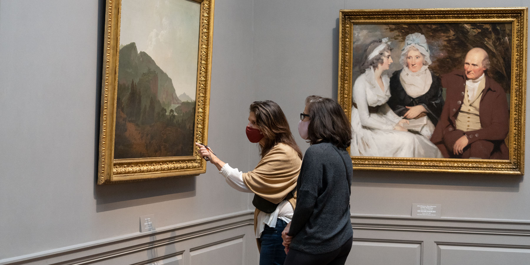 Two women wearing facemasks are looking at a painting in the National Gallery and one of them is pointing at it.
