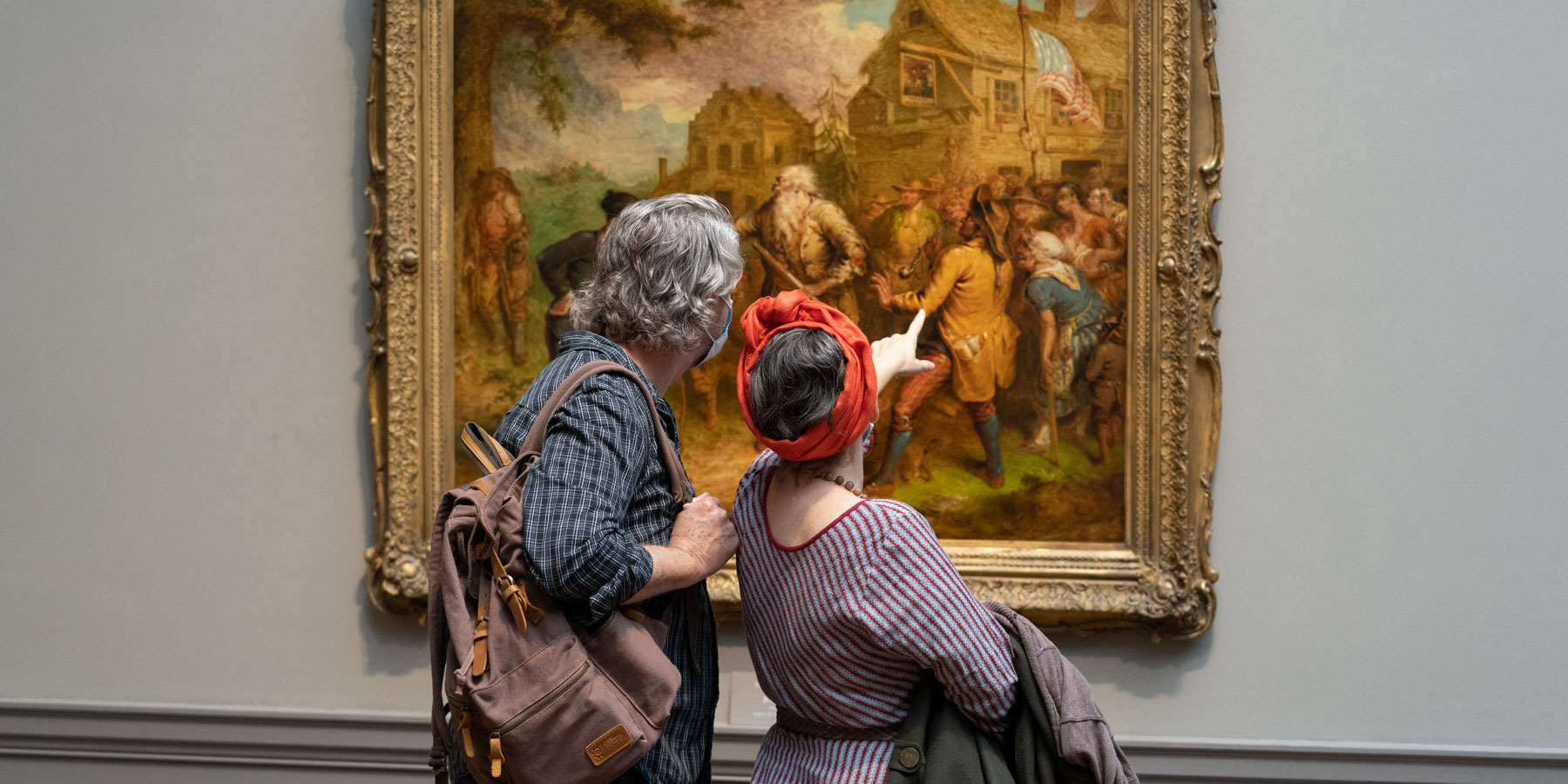 A man and a woman looking at a painting in the West Building of the National Gallery.  The woman is pointing at the painting.