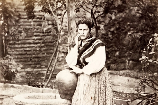A black and white photograph of a woman standing beside a well.