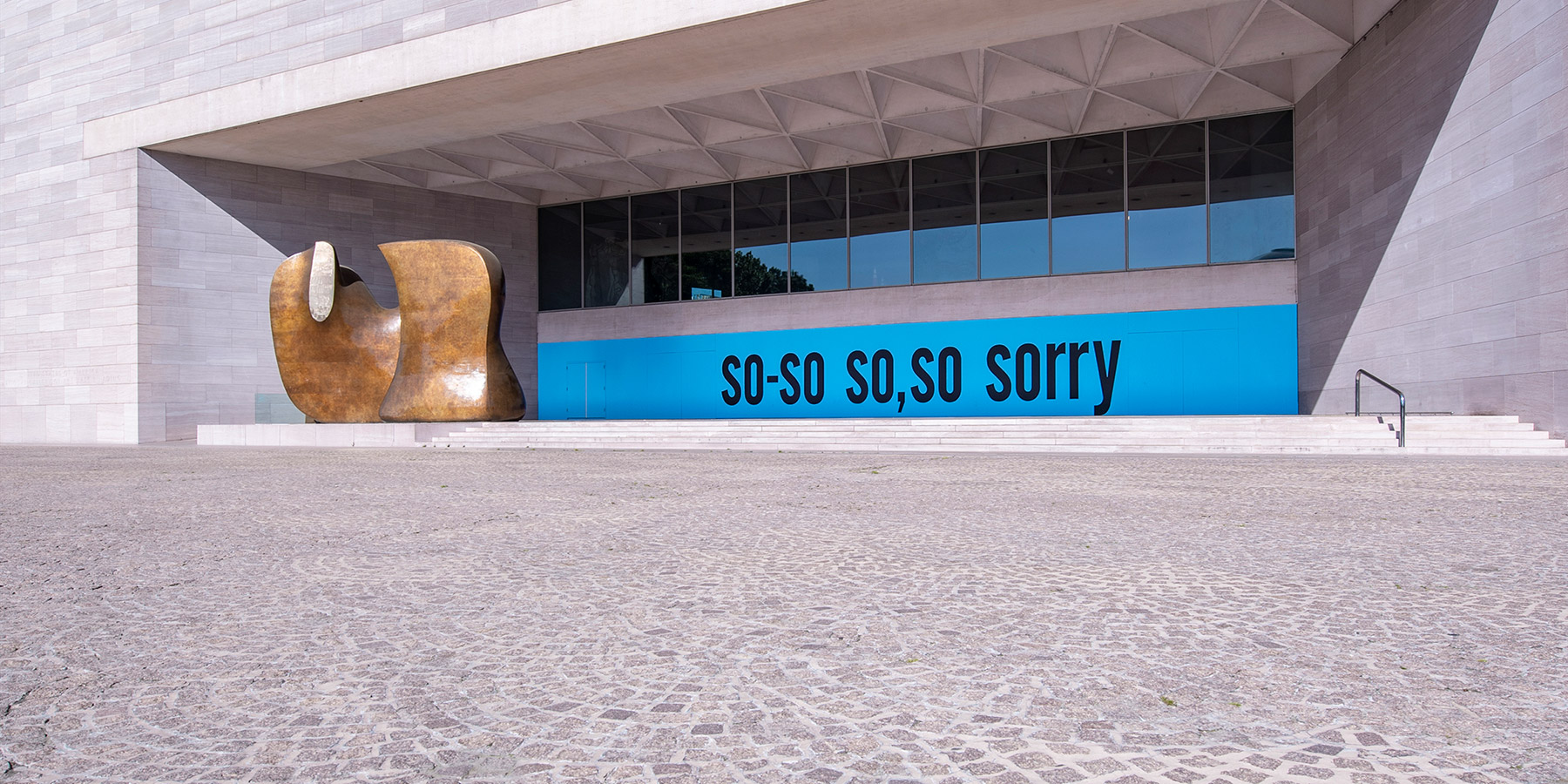 Photograph of the exeterior terrace of the East Building of the National Gallery of Art with a blue painted wall with the words so-so so, so sorry painted in black.