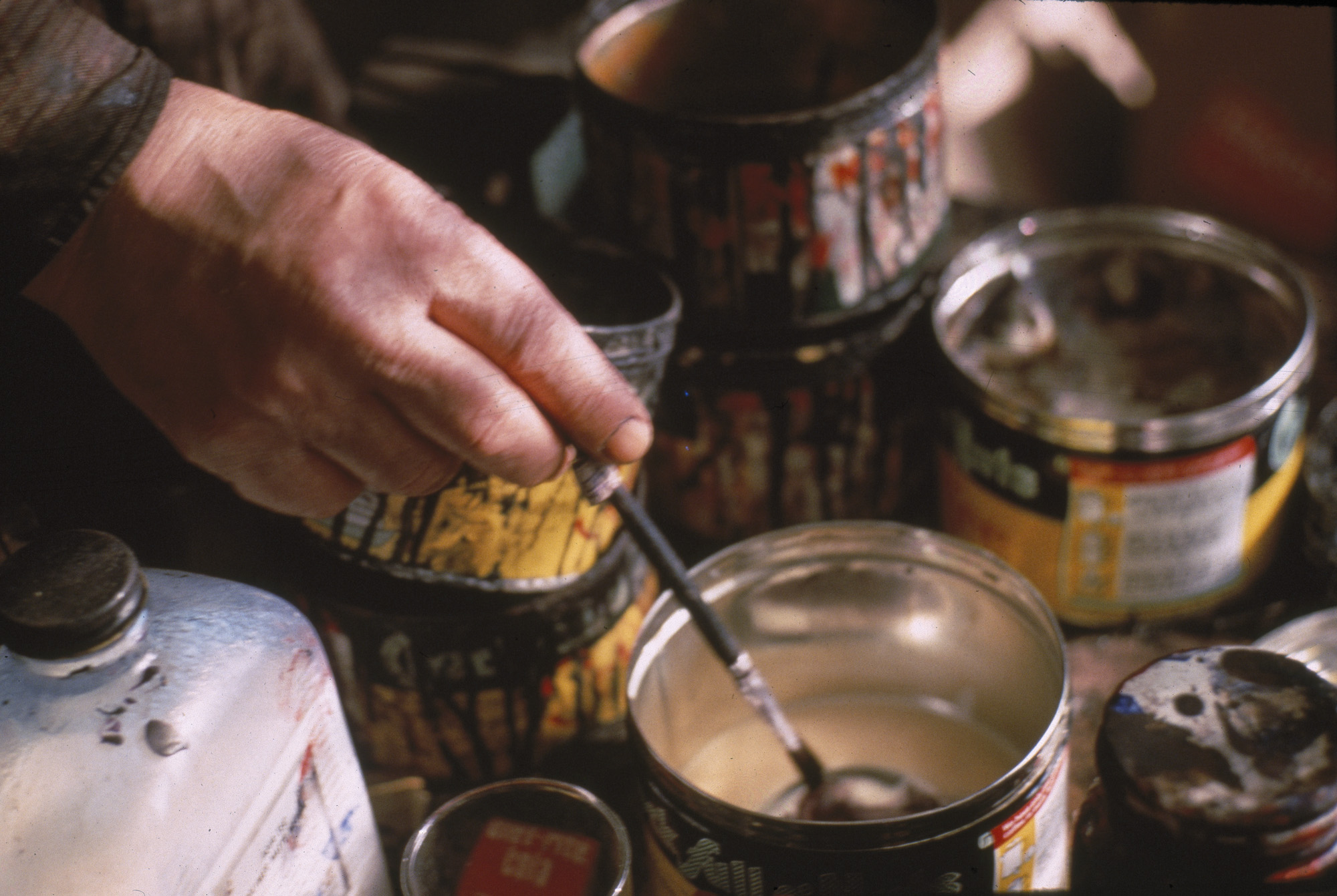 A photograph shows a beige hand holding a paintbrush in a can. 