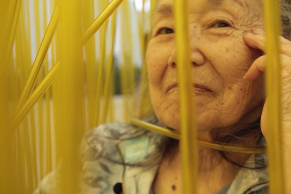 An older woman looking through tall blades of grass.