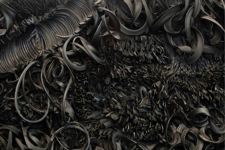 The wall-sized, horizontal sculpture consists of black rubber tires and tubing that has been sliced, stripped, woven, looped, twisted and otherwise manipulated into an expressive and abstract high-relief tableau.