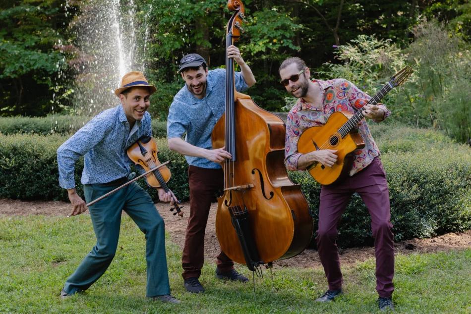 Three men playing musical instruments in a park with a water fountain behind them.