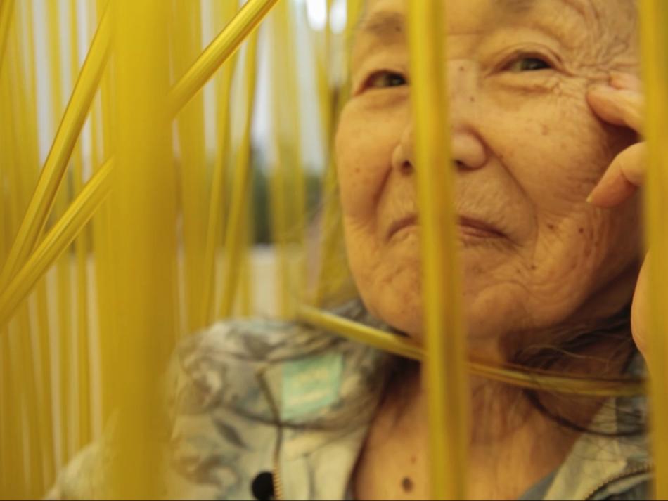 An older woman looking through tall blades of grass.