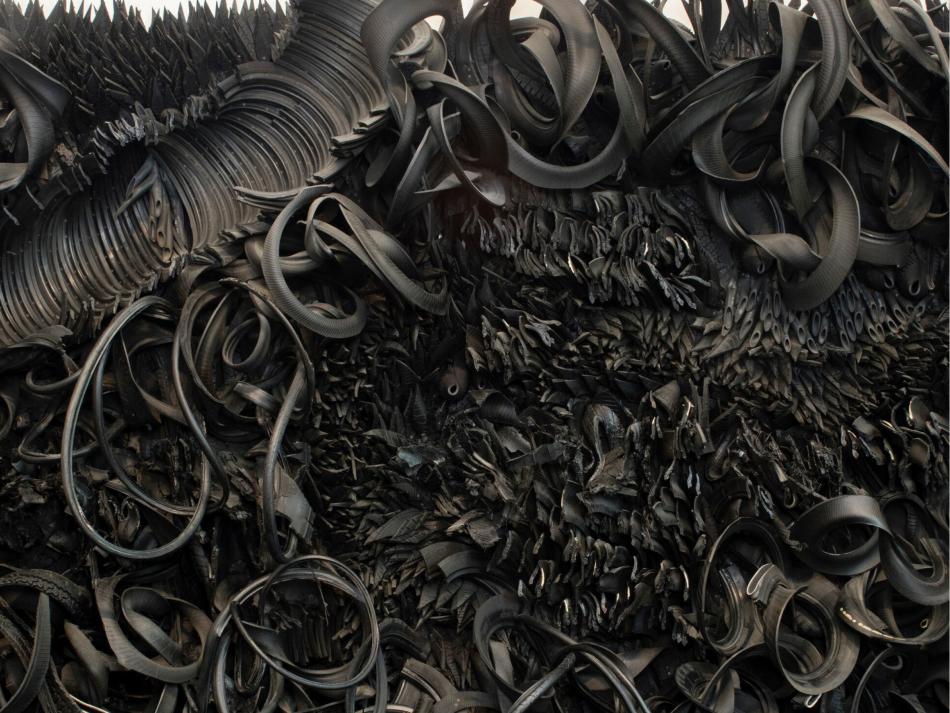 The wall-sized, horizontal sculpture consists of black rubber tires and tubing that has been sliced, stripped, woven, looped, twisted and otherwise manipulated into an expressive and abstract high-relief tableau.