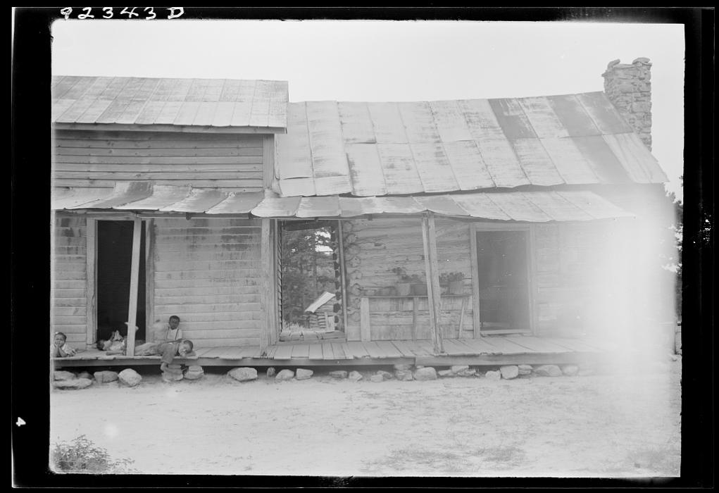 Dorothea Lange's photo of a sharecropper house in North Carolina with a Black boy seated on the porch