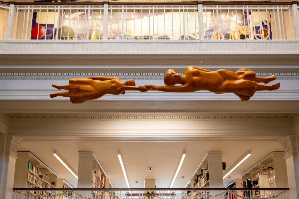 Two wood sculpted figures reach for each other over a library circulation desk