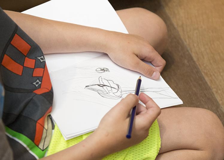 A kid sketching a drawing in a sketchbook.