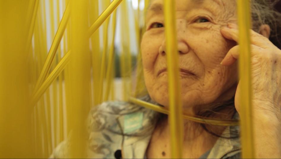 An older woman looking through tall blades of grass.