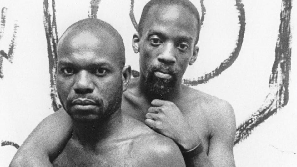 Two men without shirts on with very serious expressions on their faces.
