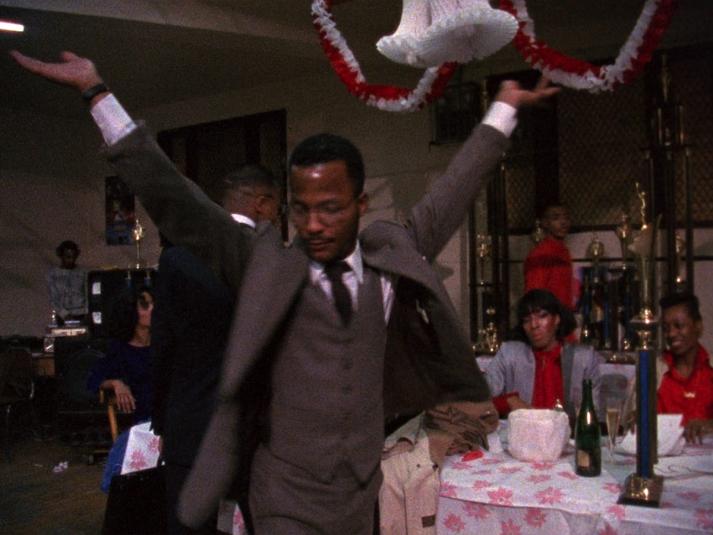 A man in a three-piece suit raising his arms.