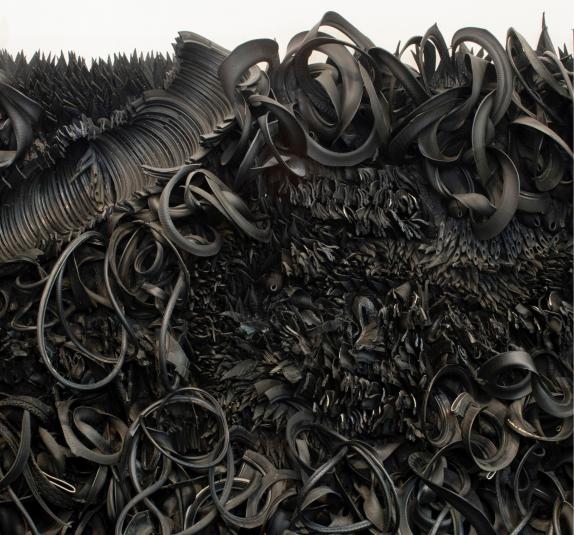 The wall-sized, horizontal sculpture consists of black rubber tires and tubing that has been sliced, stripped, woven, looped, twisted and otherwise manipulated into an expressive and abstract high-relief tableau.