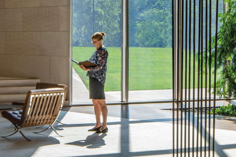 A woman standing by windows reading a book in the library