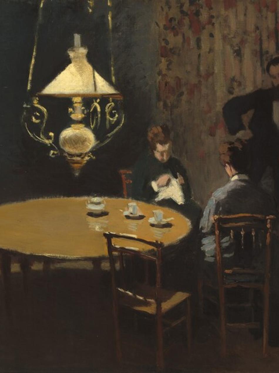There are two people sitting at a table and one person standing. They are lit by a single hanging light.They 