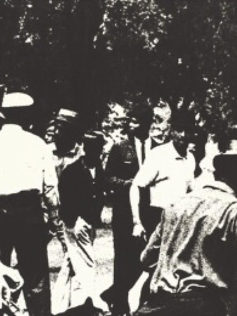 This is a black and white image of a crowd. A police officer in the foreground holds a baton and another constrains a leashed dog.