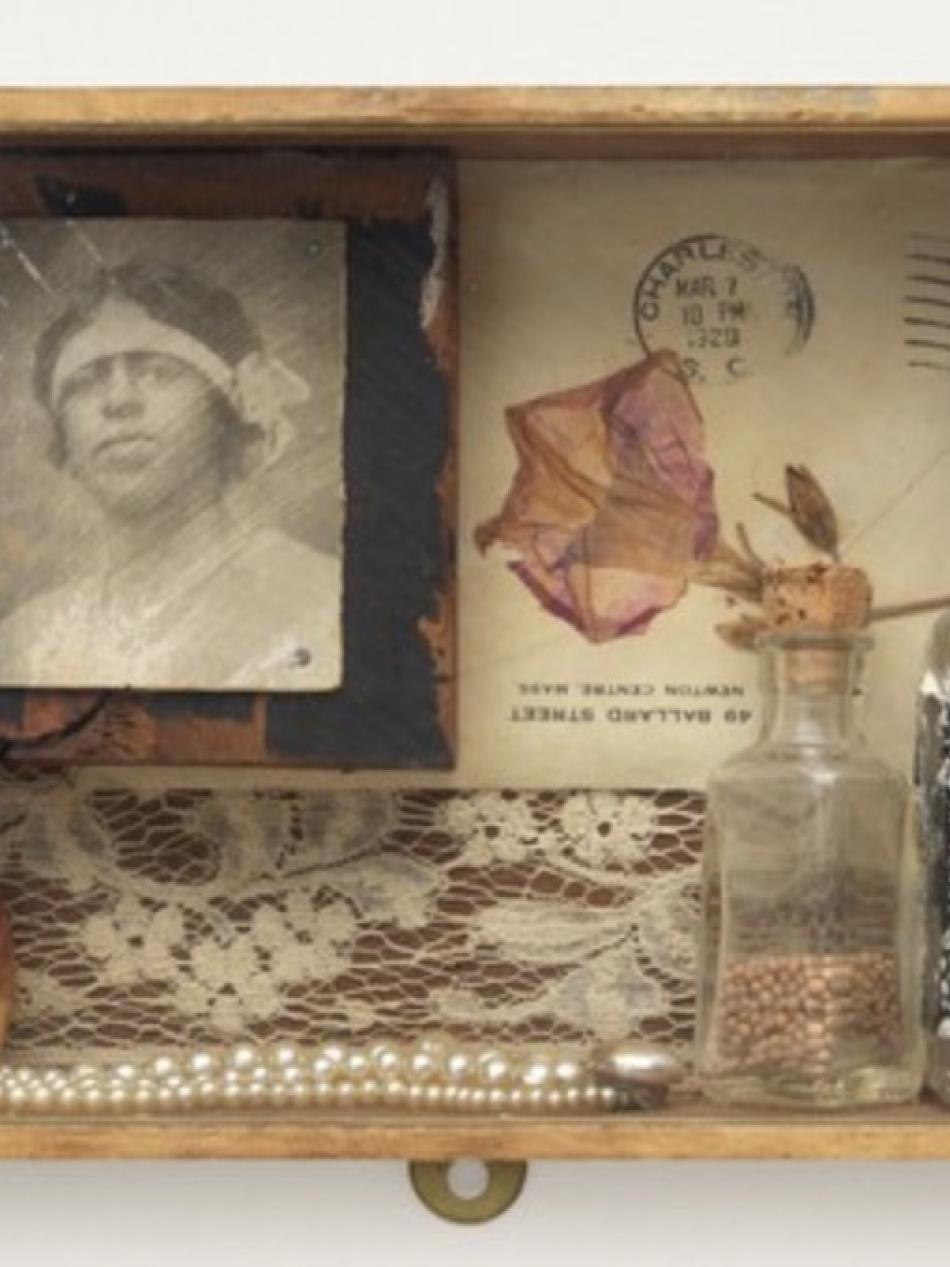 The image is looking down into a wooden box with memorabilia. It includes lace, pearl jewelry, a portrait and a bottle of whisky.