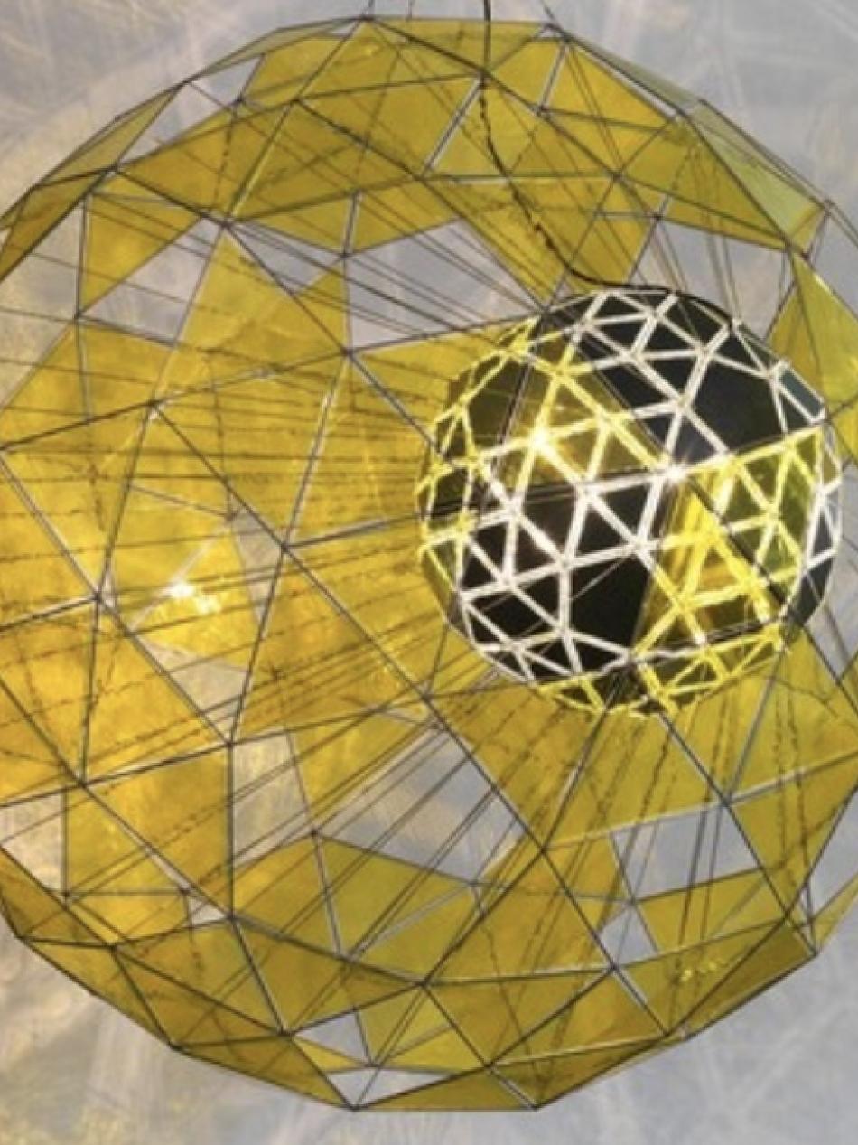 This is a sphere shaped sculpture. There are translucent gold panels of the sphere which reflect light.