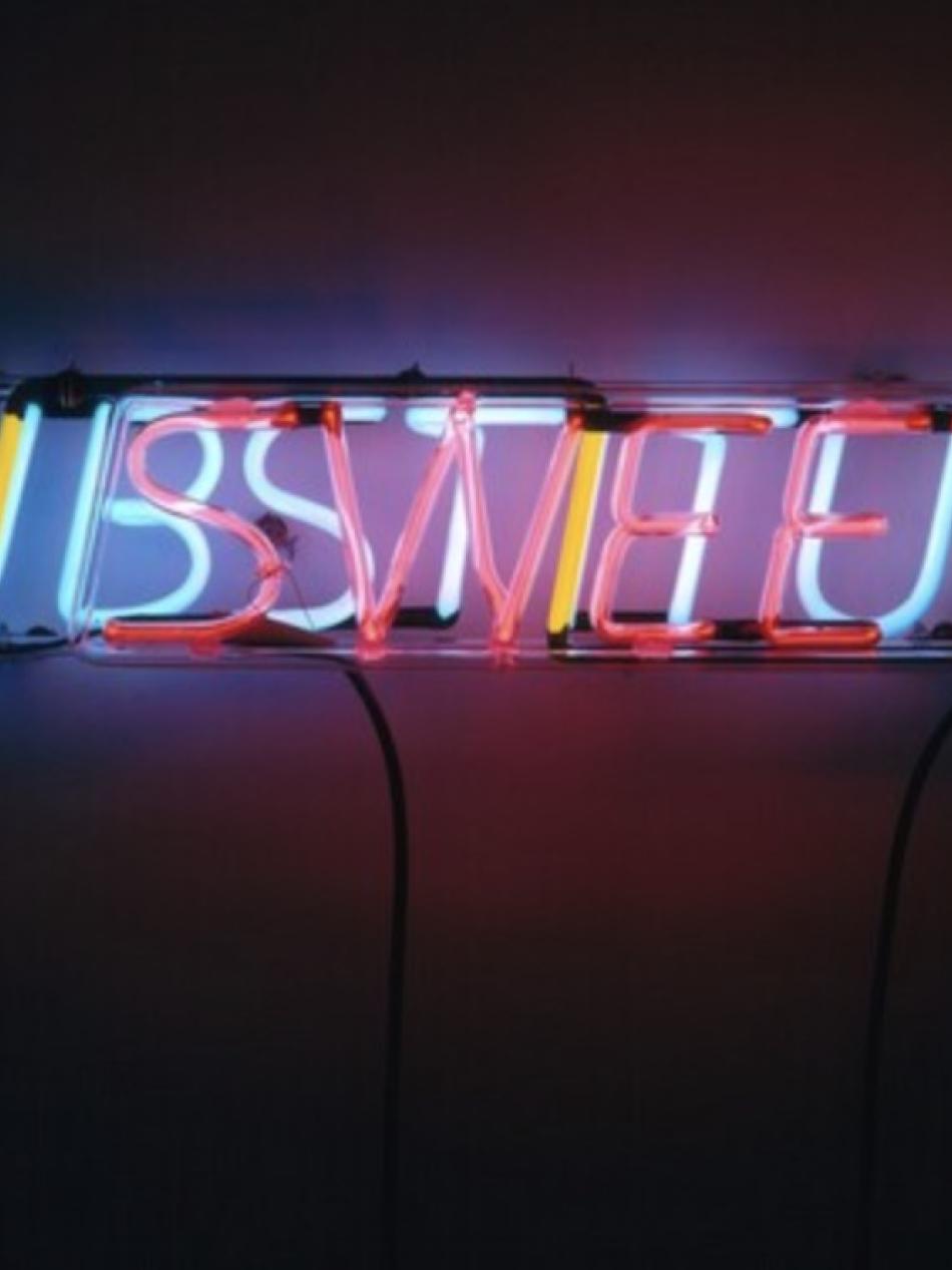 This sculpture is made of neon letters. It's hard to read but the word "sweet" is in pink neon and "substitute" in yellow.