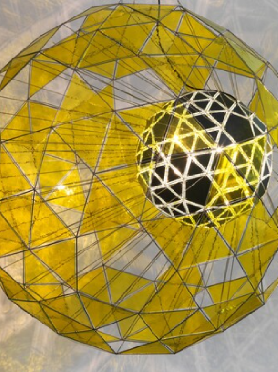 This is a sphere shaped sculpture. There are translucent gold panels of the sphere which reflect light.