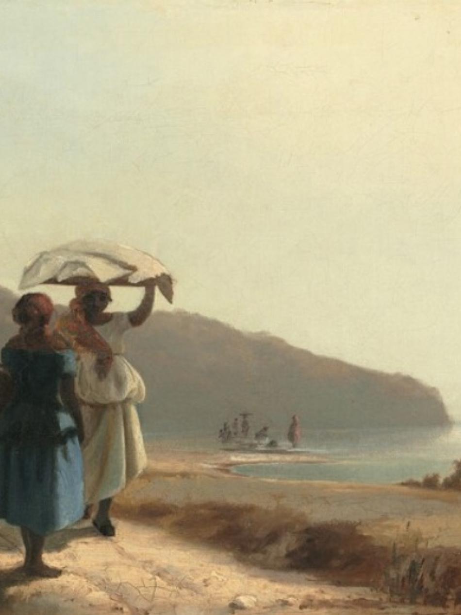 Two people are on a dirt road by the sea. There are hills in the distance behind them.